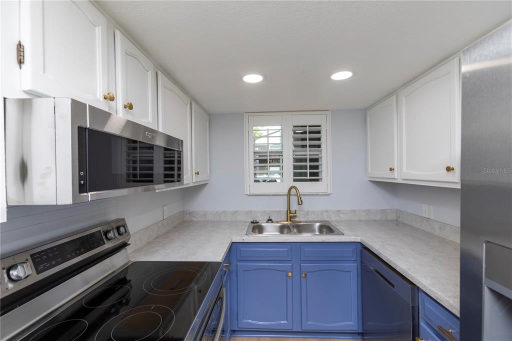 A kitchen features blue lower cabinets, white upper cabinets, stainless steel appliances, and gray countertops — 4008 PASSPORT LANE UNIT 104, NEW PORT RICHEY, FL