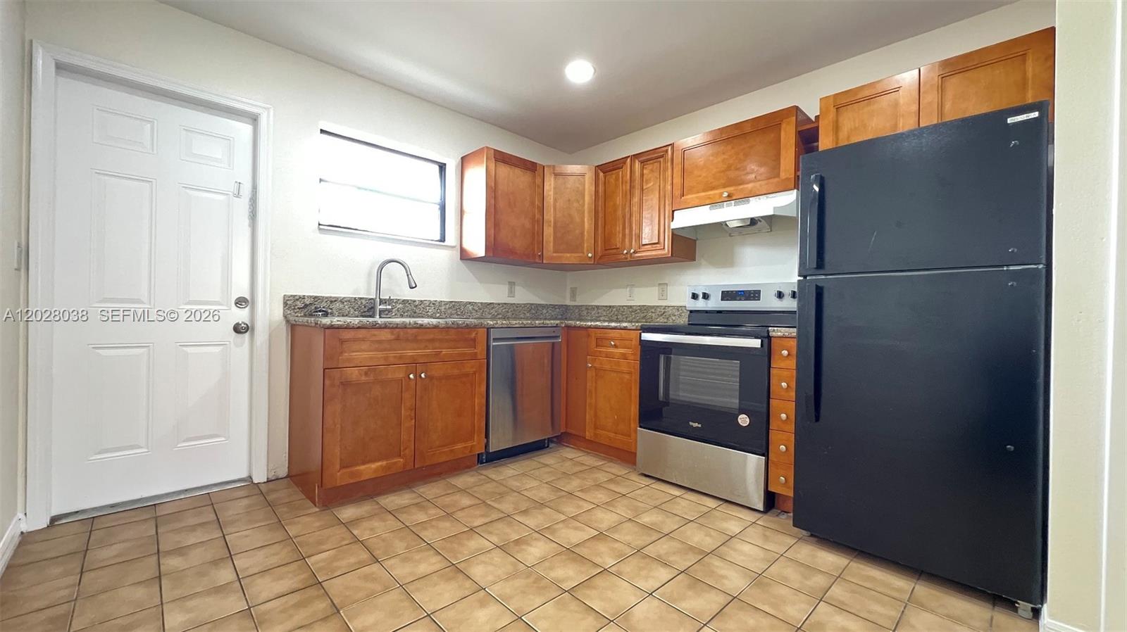 A kitchen features wood cabinets, granite countertops, stainless steel appliances, and a black refrigerator — 5914 Taylor St # 2, Hollywood FL 33021, HOLLYWOOD, FL