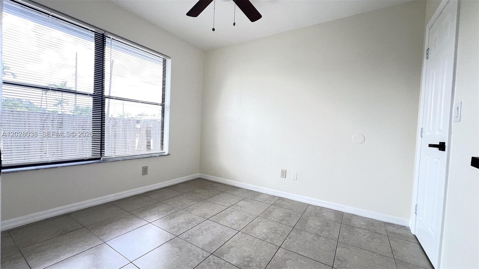 An empty room features light-colored walls, gray tile flooring, a ceiling fan, and a window — 5914 Taylor St # 2, Hollywood FL 33021, HOLLYWOOD, FL