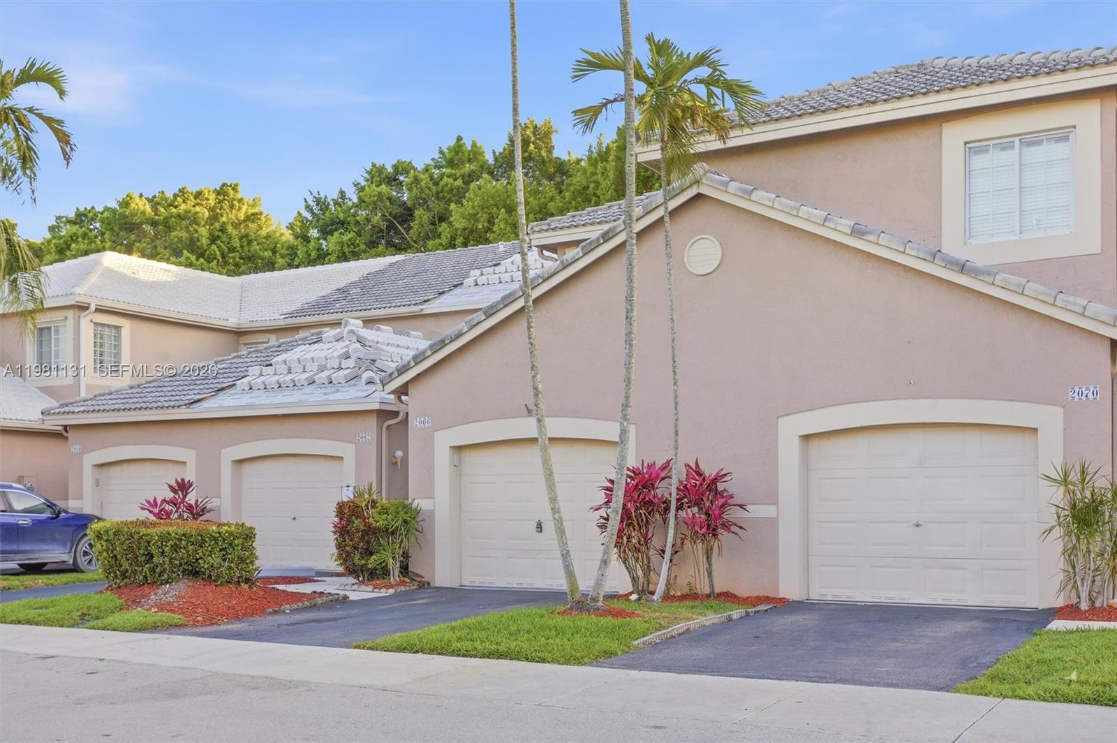 A row of attached townhouses features beige stucco walls, tiled roofs, and individual garage doors — 2066 Madeira Dr # 2066, Weston FL 33327, WESTON, FL