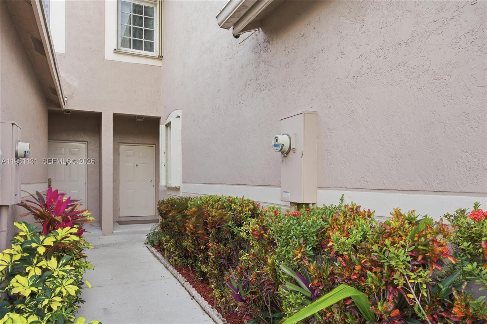 A concrete walkway leads to two beige doors beside a wall with a utility meter — 2066 Madeira Dr # 2066, Weston FL 33327, WESTON, FL