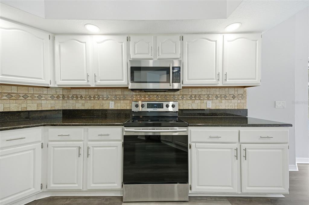 A kitchen with white cabinets, dark granite countertops, stainless steel appliances, and a tiled backsplash — 504 STRATFIELD DRIVE, LUTZ, FL