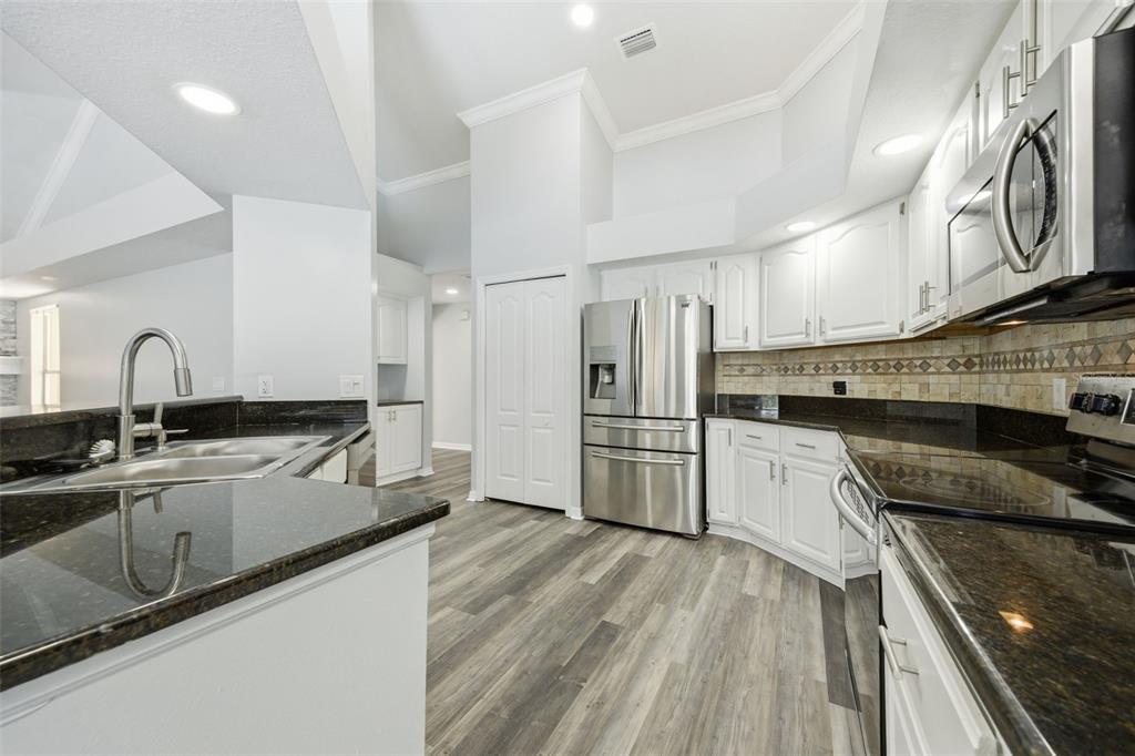 A kitchen features white cabinets, dark granite countertops, stainless steel appliances, and wood-look flooring — 504 STRATFIELD DRIVE, LUTZ, FL