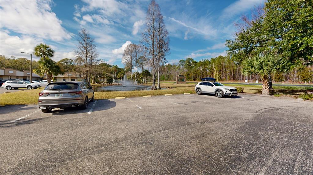 A parking lot with two cars sits in front of a pond with a fountain — 605 NW 53RD AVENUE UNIT A-18, GAINESVILLE, FL