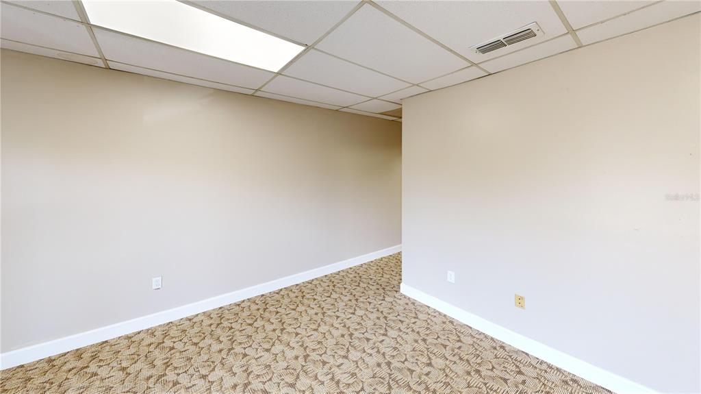 An empty office room features beige walls, a patterned carpet, and a drop ceiling — 605 NW 53RD AVENUE UNIT A-18, GAINESVILLE, FL