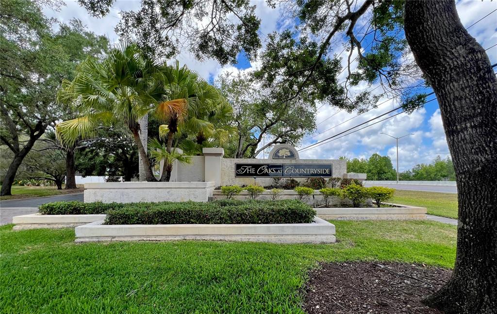 A stone monument sign for The Oaks at Countryside stands amidst landscaping and large trees — 3014 RED OAK COURT UNIT 102, PALM HARBOR, FL