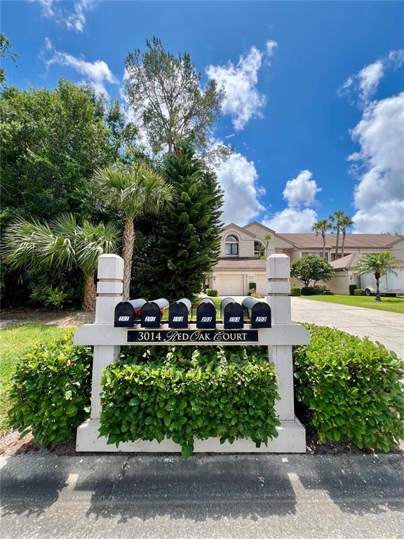 A row of six mailboxes sits on a white wooden stand in front of a house — 3014 RED OAK COURT UNIT 102, PALM HARBOR, FL