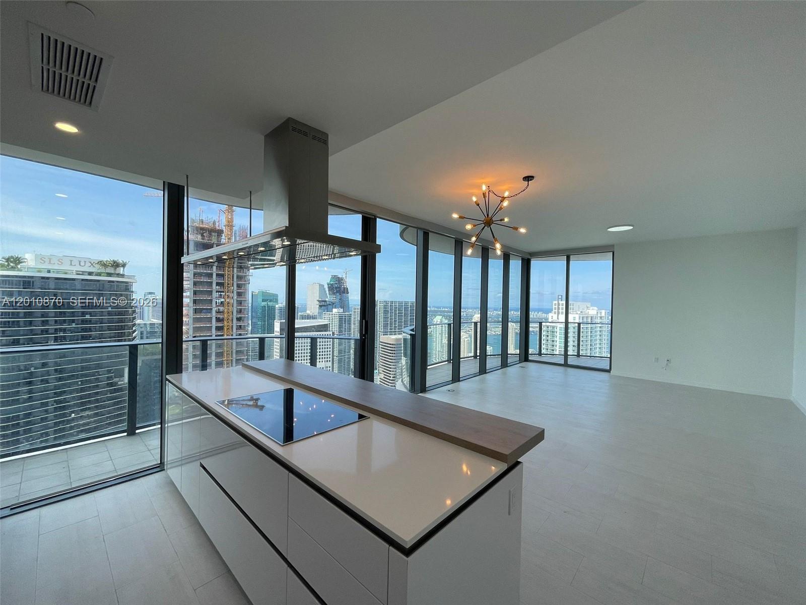 A modern kitchen island with a cooktop sits in an open-plan room with floor-to-ceiling windows — 1000 Brickell Plaza # 5908, Miami FL 33131, MIAMI, FL