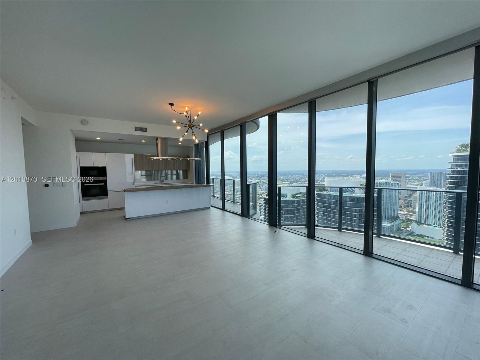A modern open-concept kitchen and living area features floor-to-ceiling windows with expansive city views — 1000 Brickell Plaza # 5908, Miami FL 33131, MIAMI, FL