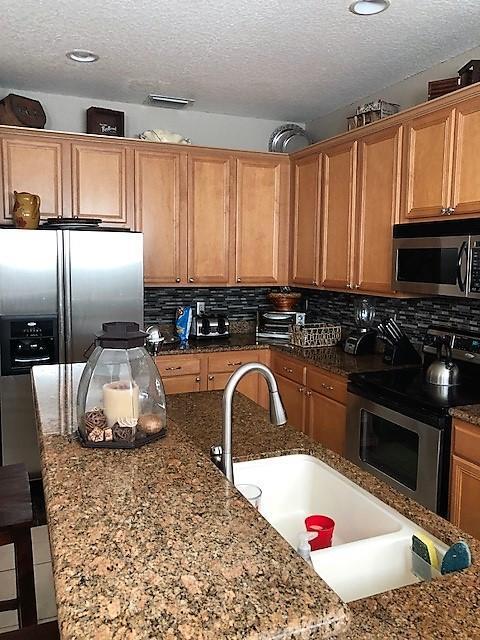 A kitchen features wood cabinets, granite countertops, a stainless steel refrigerator, and a double sink — 118 Ocean Cay Way, Hypoluxo FL 33462, HYPOLUXO, FL