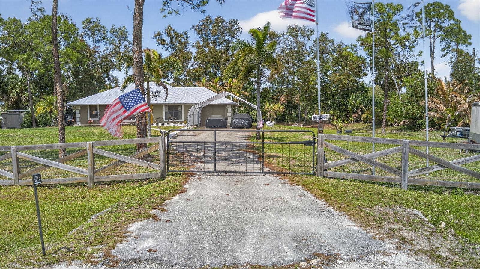 A single-story house with a metal roof sits behind a wooden fence and gated driveway — 17815 92nd Lane N, FL 33470, FL