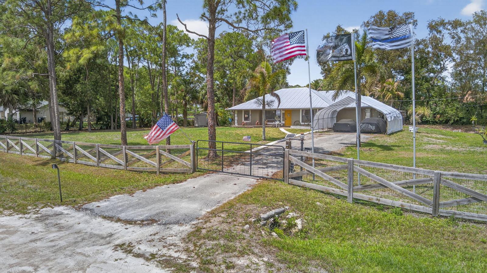 A single-story house with a metal carport, a fenced yard, and several flags on poles — 17815 92nd Lane N, FL 33470, FL