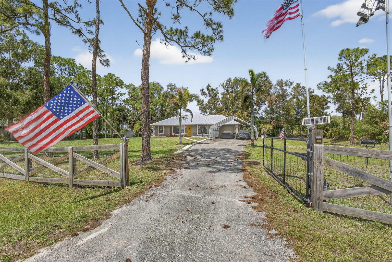 A gravel driveway leads to a single-story house with a metal carport and wooden fencing — 17815 92nd Lane N, FL 33470, FL