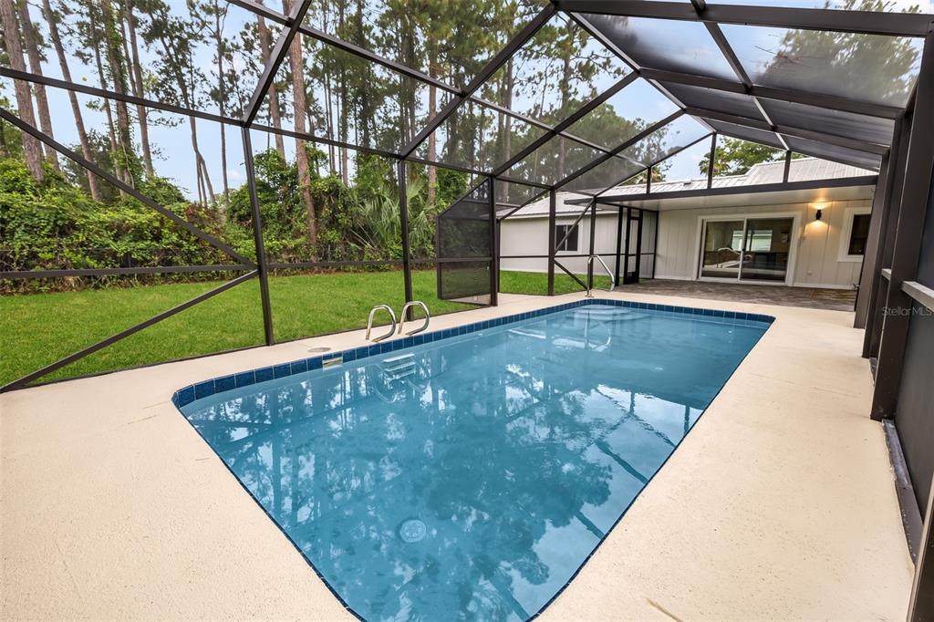 A swimming pool sits inside a screened-in lanai next to a house and grassy yard — 114 BEACON MILL LANE, PALM COAST, FL