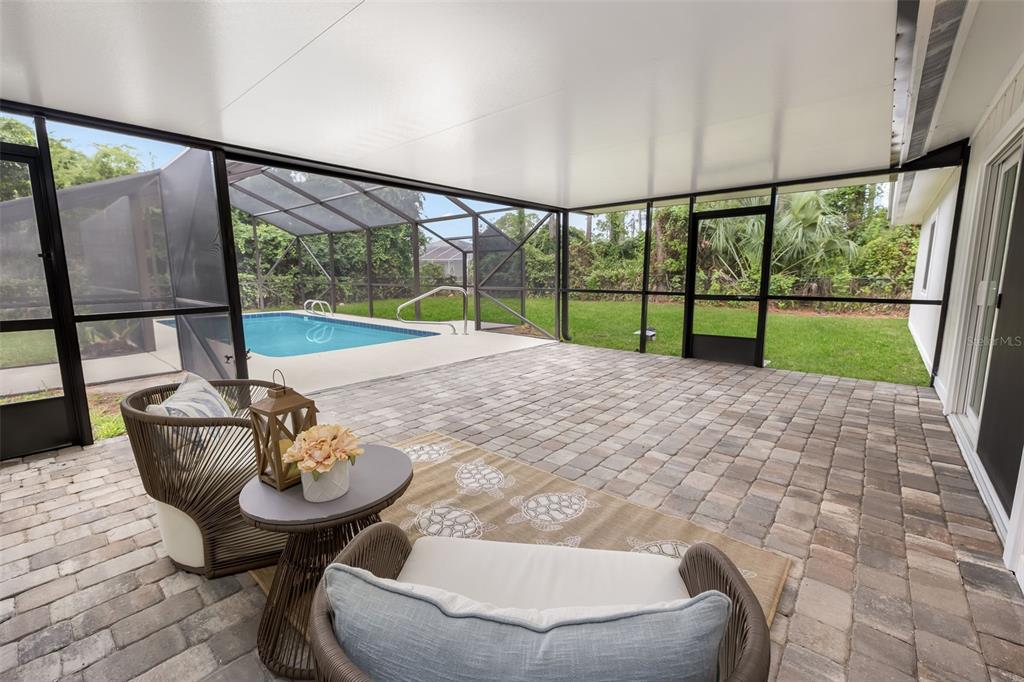 A covered patio with paver flooring overlooks a screened-in swimming pool and a grassy backyard — 114 BEACON MILL LANE, PALM COAST, FL