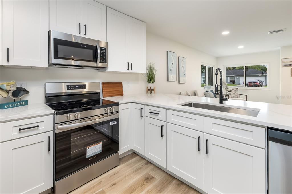 A modern kitchen features white cabinets, stainless steel appliances, and white countertops — 114 BEACON MILL LANE, PALM COAST, FL