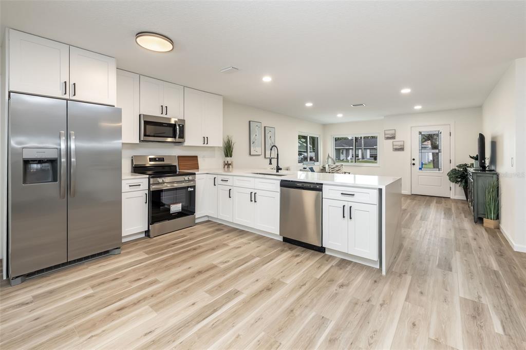 A modern kitchen features white cabinets, stainless steel appliances, and light wood-look flooring — 114 BEACON MILL LANE, PALM COAST, FL