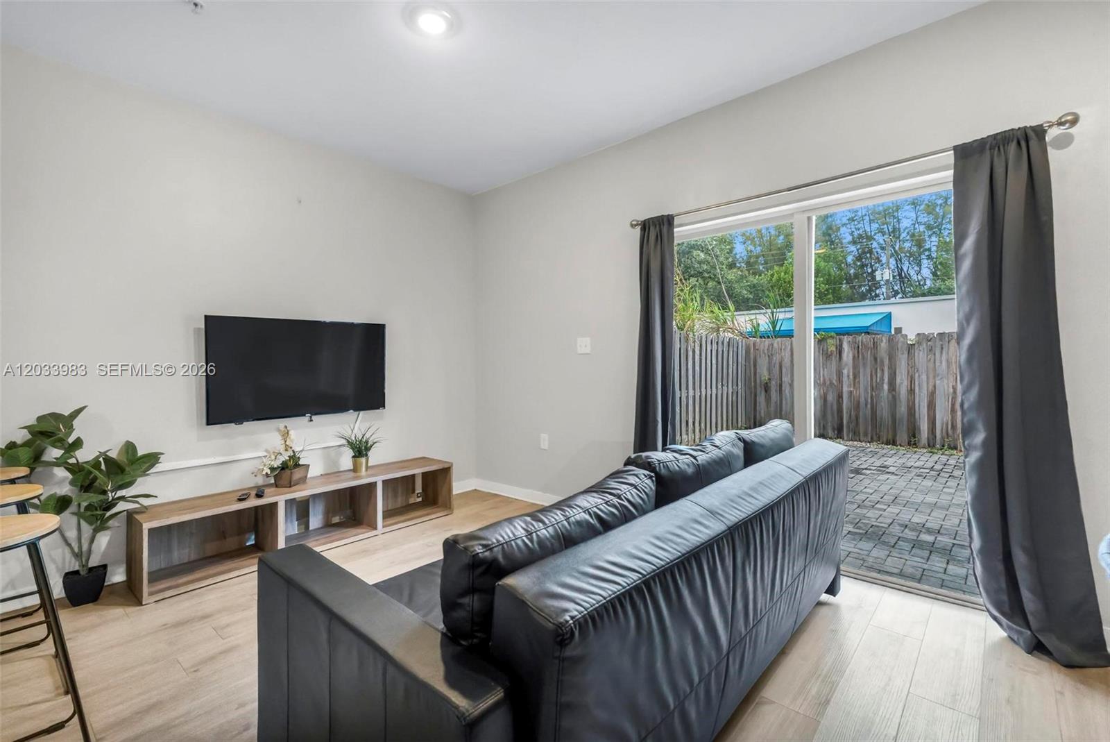 A living room features a black sofa, a wall-mounted television, and a sliding glass door — 171 NW 158th St # 10, Miami FL 33169, MIAMI, FL