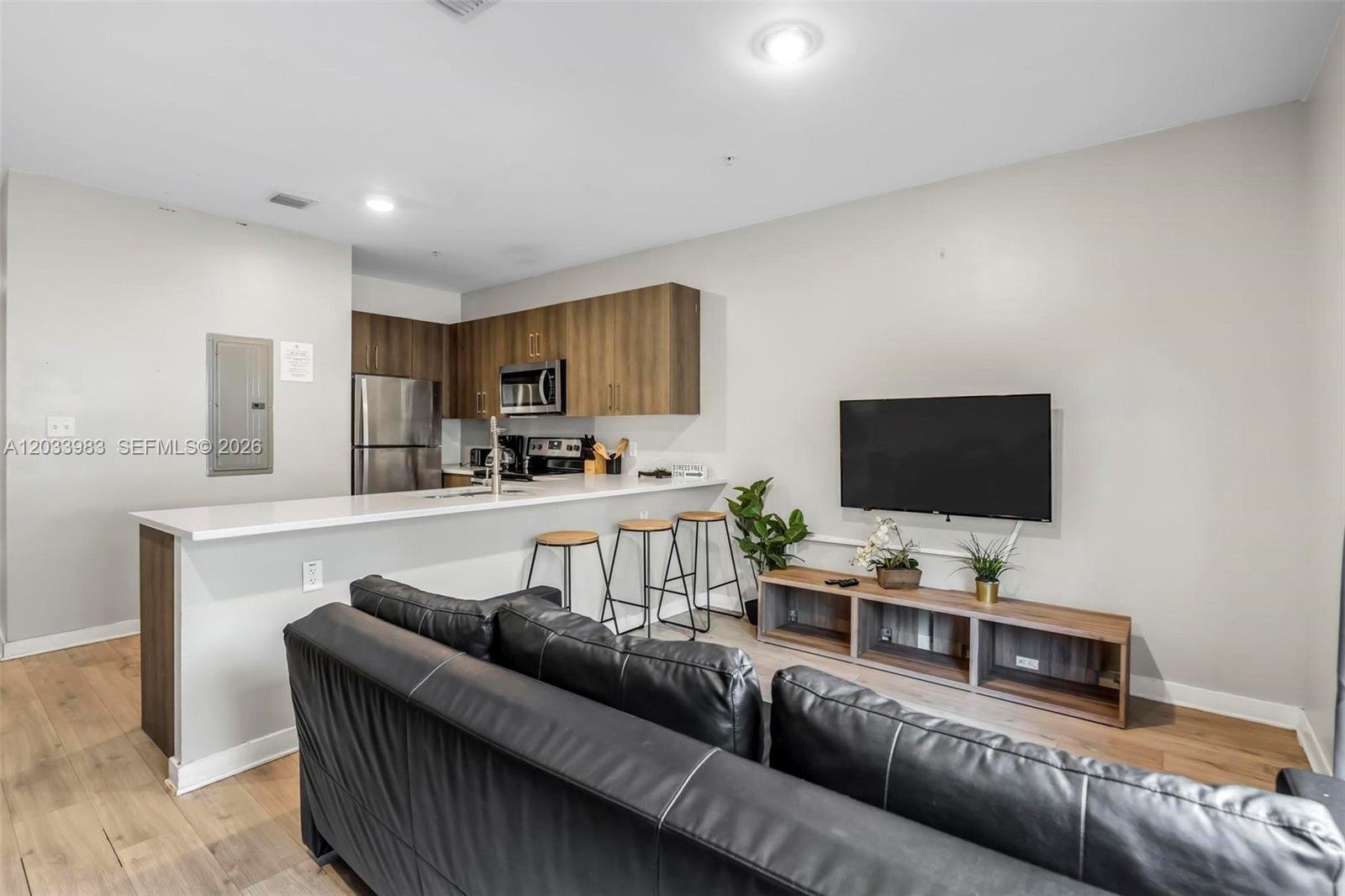 A living room with a black leather sofa faces a television mounted above a wooden console — 171 NW 158th St # 10, Miami FL 33169, MIAMI, FL