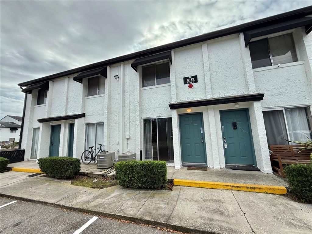 A two-story apartment building exterior with white stucco walls, teal doors, and a parking lot — 4113 S SEMORAN BOULEVARD UNIT 14, ORLANDO, FL