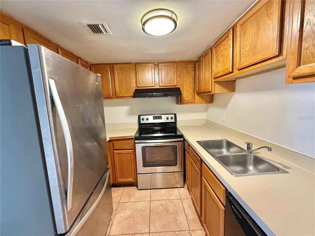 A galley kitchen features wood cabinets, stainless steel appliances, and light-colored countertops — 4113 S SEMORAN BOULEVARD UNIT 14, ORLANDO, FL