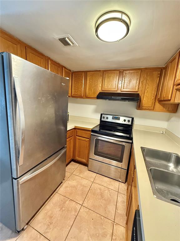 A kitchen features stainless steel appliances, wood cabinets, and light-colored countertops over tiled floors — 4113 S SEMORAN BOULEVARD UNIT 14, ORLANDO, FL