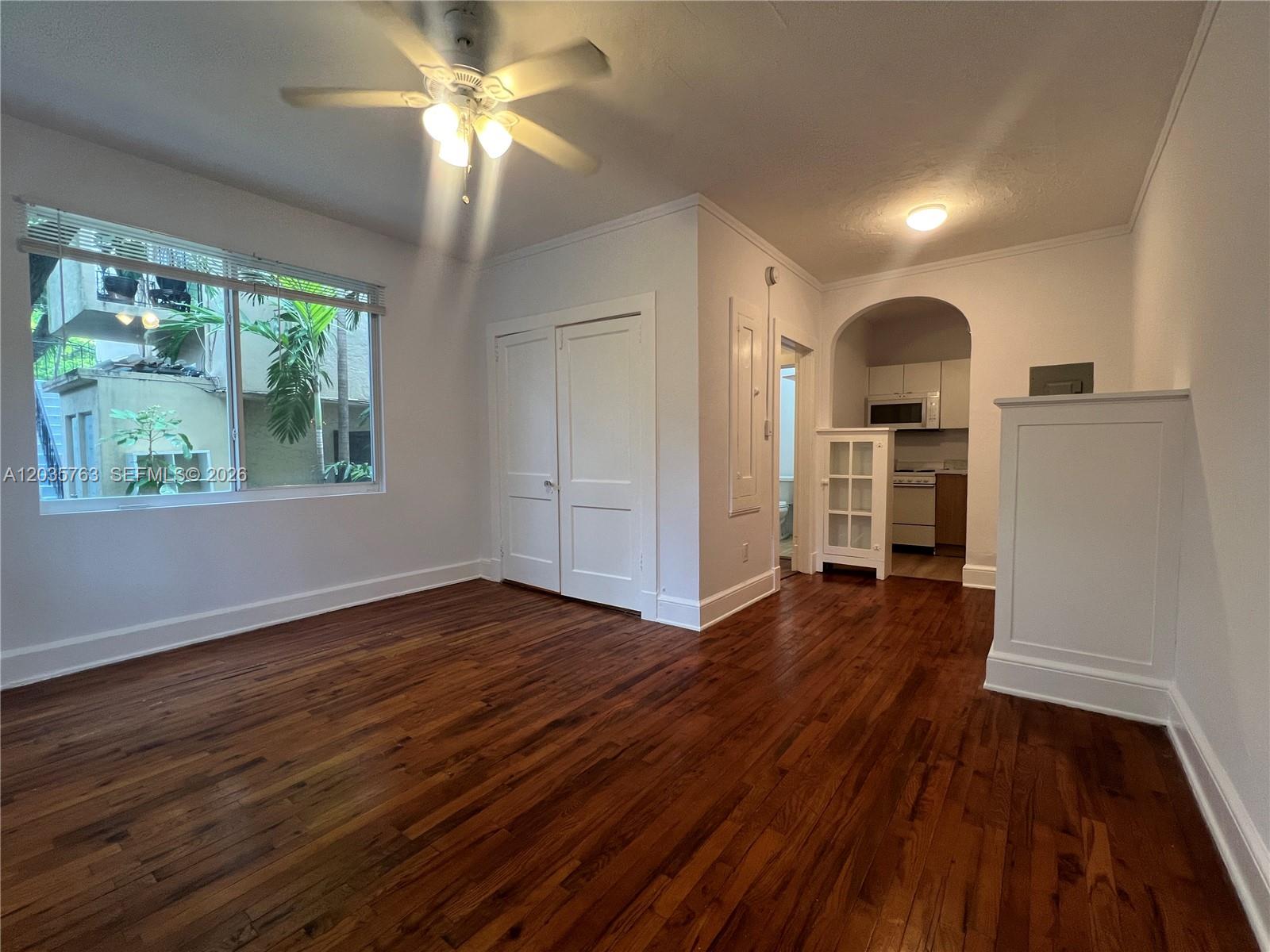 An empty room features dark hardwood floors, a ceiling fan, and an arched kitchen entrance — 1610 Salzedo St # 5, Coral Gables FL 33134, CORAL GABLES, FL
