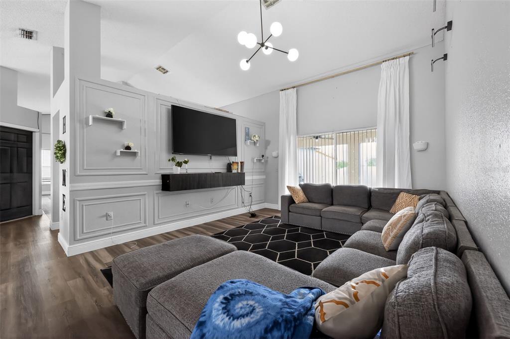 A living room features a gray sectional sofa, a wall-mounted television, and decorative wall molding — 7938 ASHLEY POINTE DRIVE, LAKELAND, FL