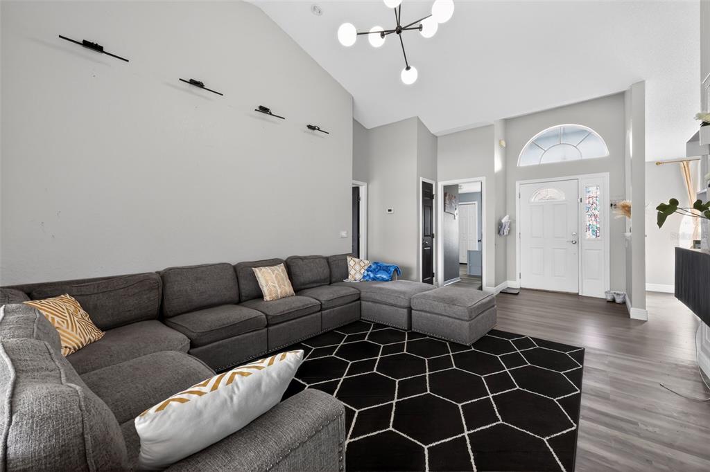 A living room features a large grey sectional, a geometric rug, and a vaulted ceiling — 7938 ASHLEY POINTE DRIVE, LAKELAND, FL