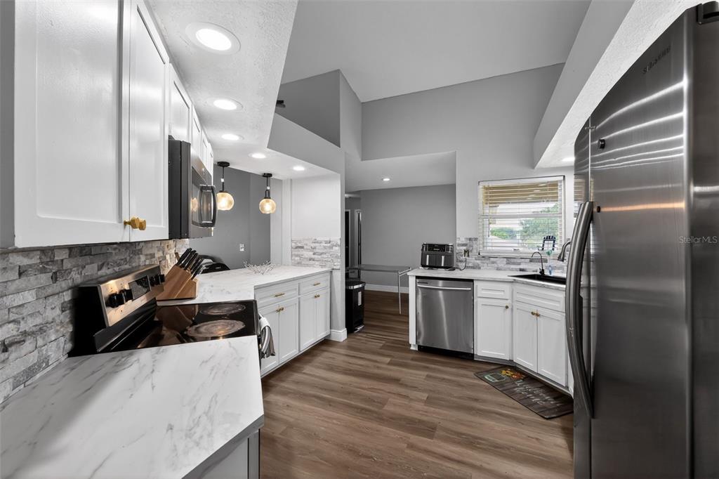 A kitchen features white cabinets, marble-look countertops, stainless steel appliances, and wood-style flooring — 7938 ASHLEY POINTE DRIVE, LAKELAND, FL