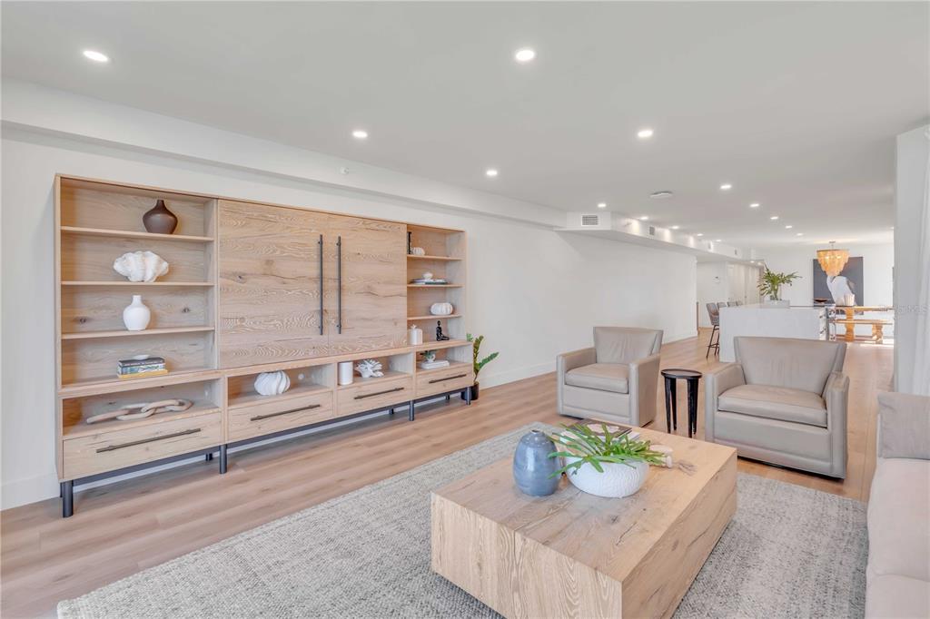 A modern living room features light wood flooring, a large built-in shelving unit, and two armchairs — 5611 GULF OF MEXICO DRIVE UNIT 1, LONGBOAT KEY, FL