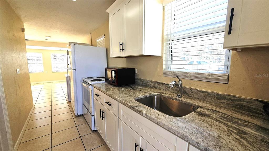 A kitchen features white cabinets, granite countertops, a stainless steel sink, and white appliances — 870 S MCCALL ROAD UNIT 4, ENGLEWOOD, FL