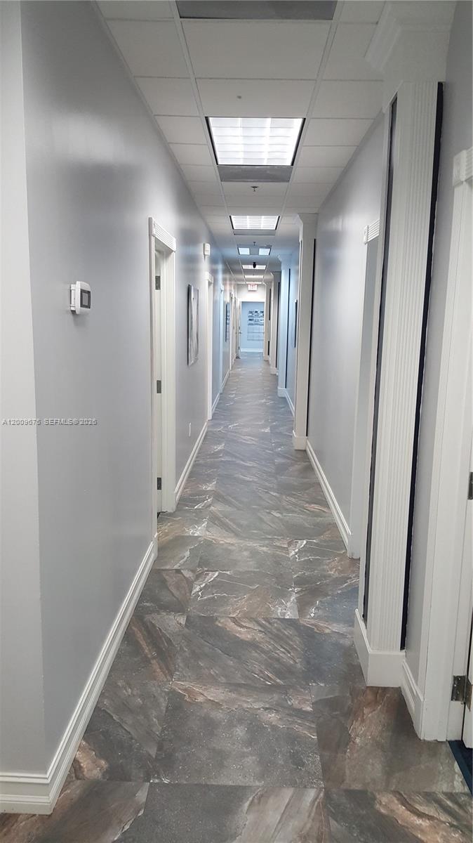 A long office hallway features gray walls, a drop ceiling, and dark marble-patterned tile flooring — 7500 NW 25th St # 114, Miami FL 33122, MIAMI, FL