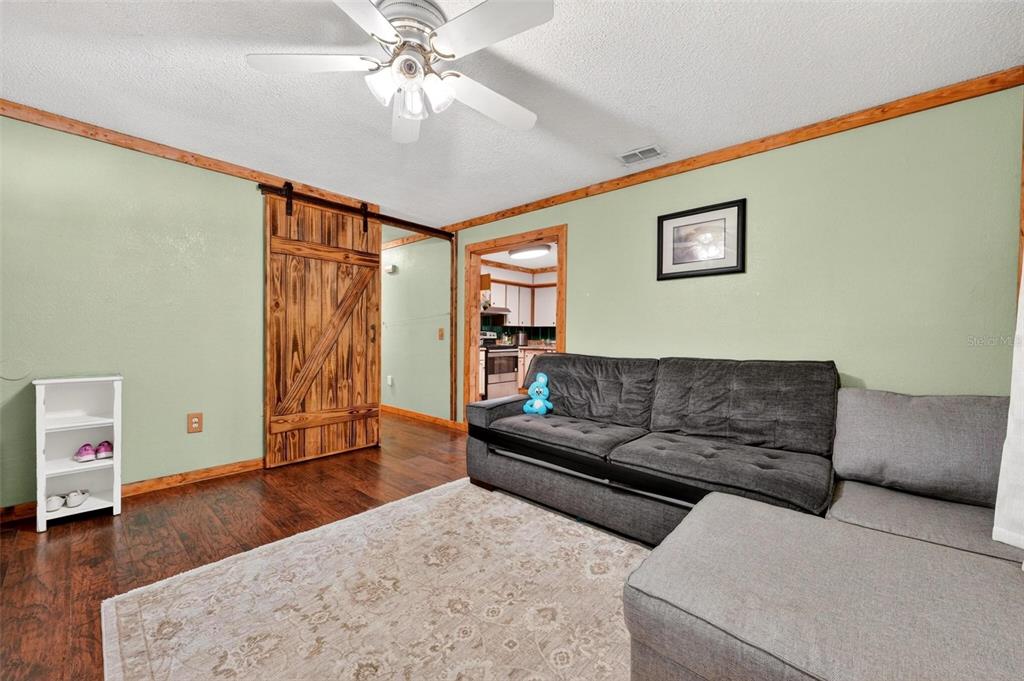 A living room with light green walls, wood trim, a barn door, and a gray sectional — 715 4TH STREET, POLK CITY, FL