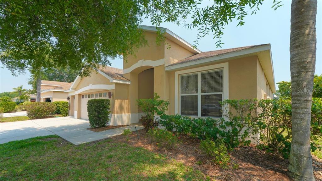 A tan single-story house with a two-car garage and a landscaped front yard — 5453 NEW COVINGTON DRIVE, SARASOTA, FL