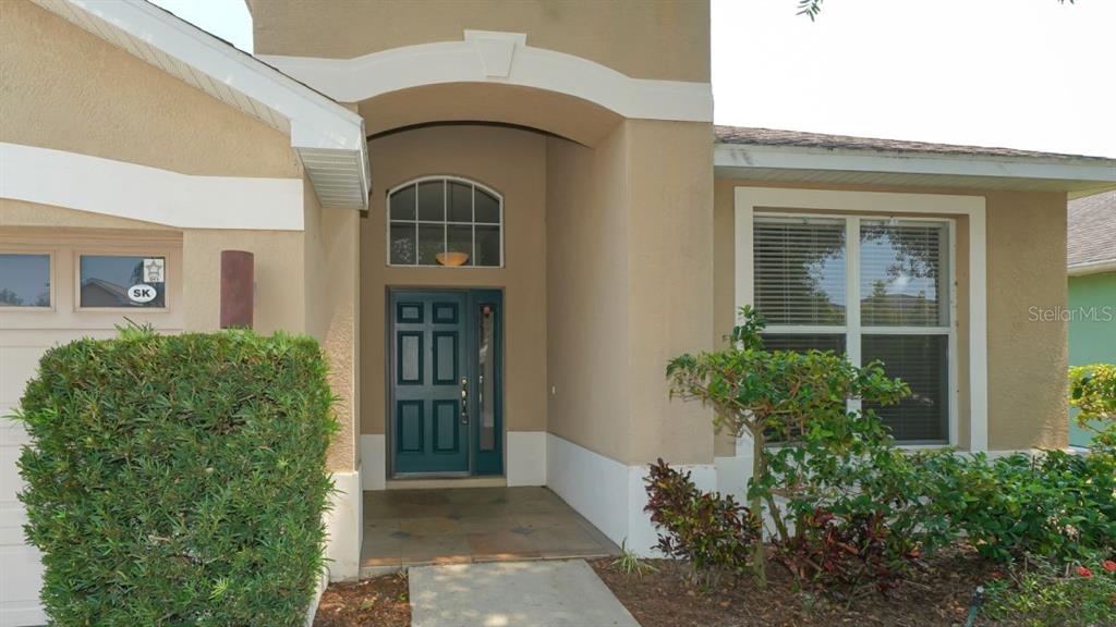 The exterior of a tan house features a covered entryway with a dark front door — 5453 NEW COVINGTON DRIVE, SARASOTA, FL