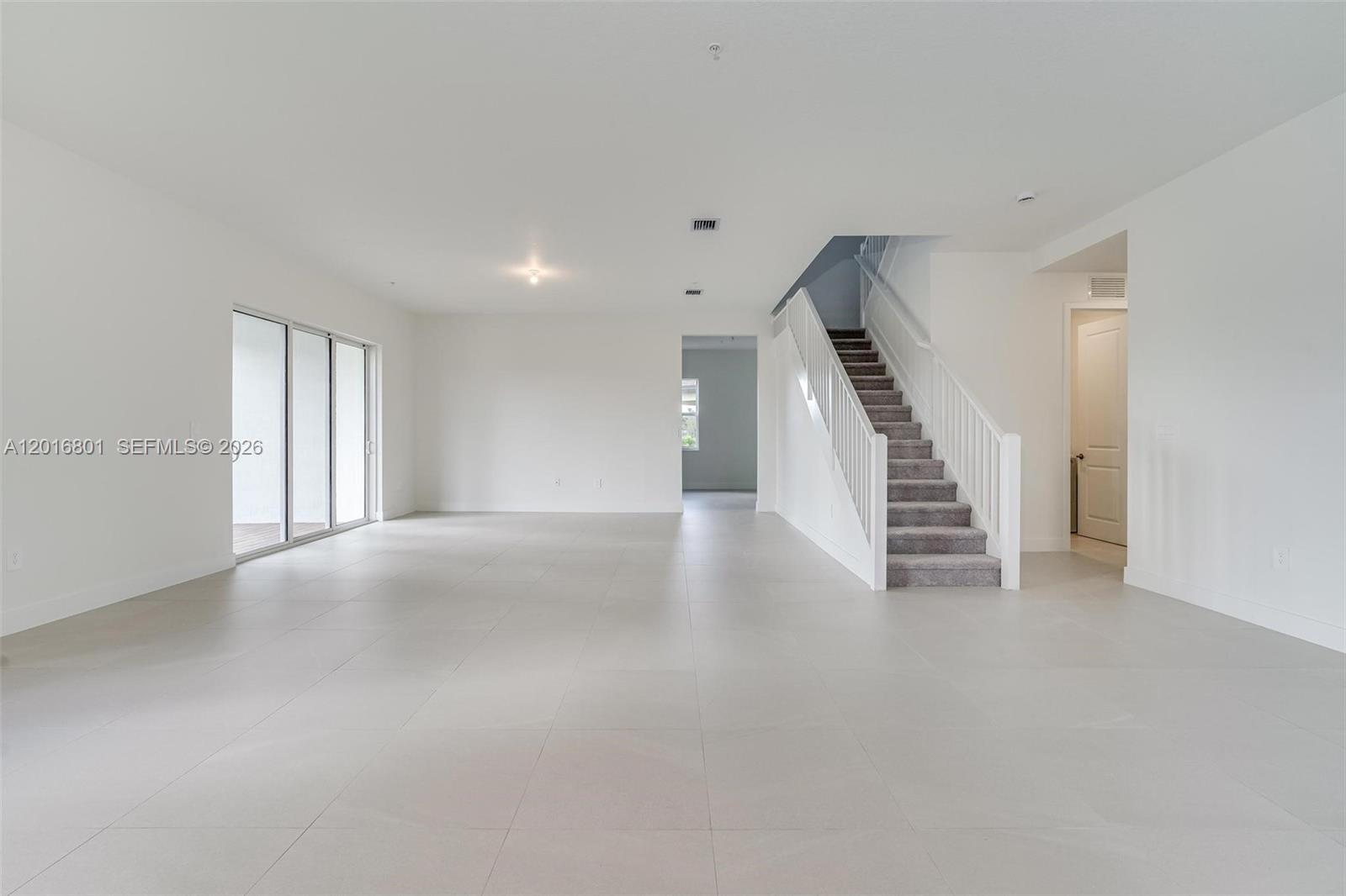 An empty room with light tile flooring, white walls, and a carpeted staircase — 4480 SW 122nd Ter # 0, Davie FL 33330, DAVIE, FL