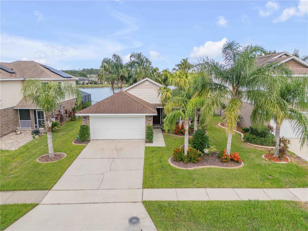 A single-story house with a white garage, palm trees, and a lake in the background — 5410 CORDGRASS BEND LANE, PORT ORANGE, FL