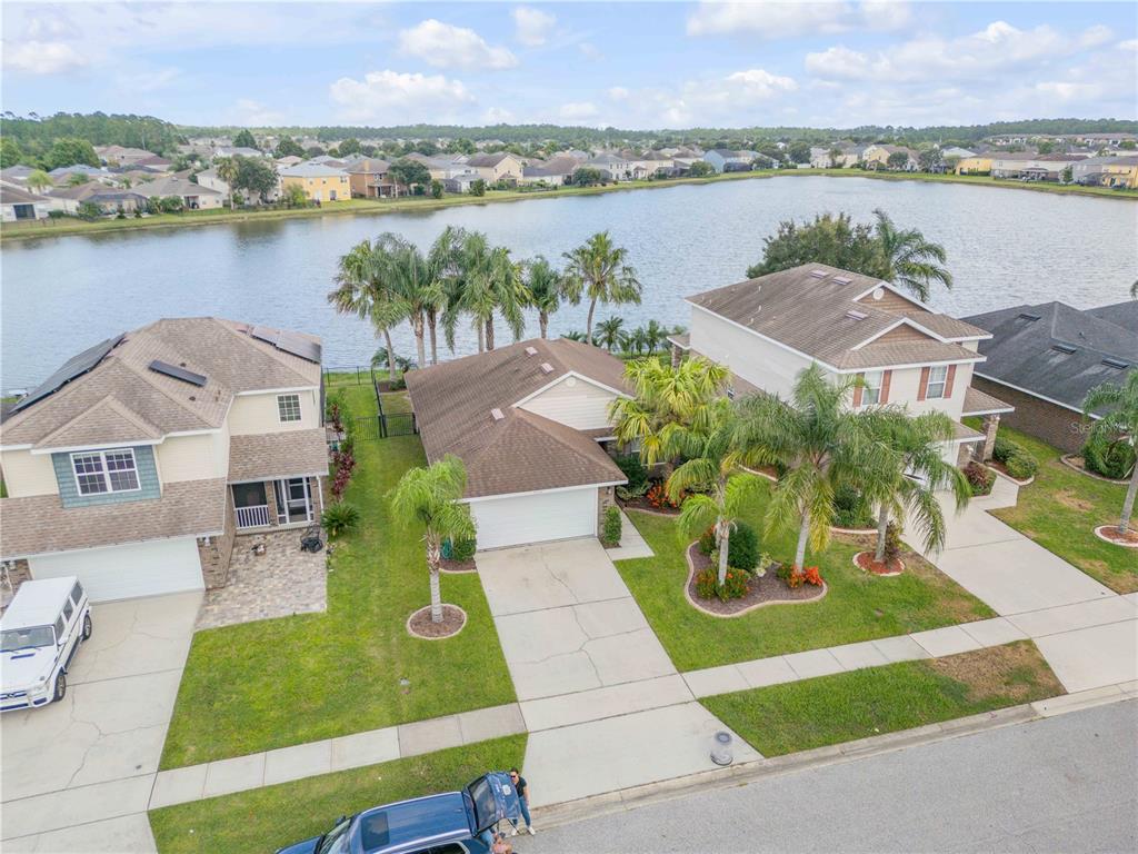 An aerial view shows three suburban houses situated along the edge of a large lake — 5410 CORDGRASS BEND LANE, PORT ORANGE, FL