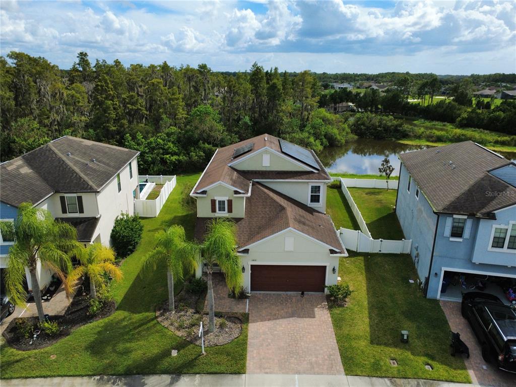 An aerial view of a two-story suburban house with solar panels and a backyard pond — 11832 LAKE BOULEVARD, NEW PORT RICHEY, FL
