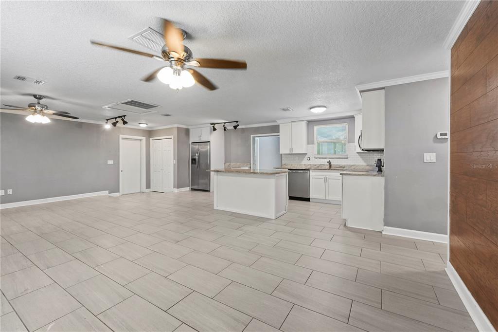A kitchen with white cabinets, granite countertops, and tile flooring opens into a living area — 6290 PIEDMONT DRIVE, SPRING HILL, FL