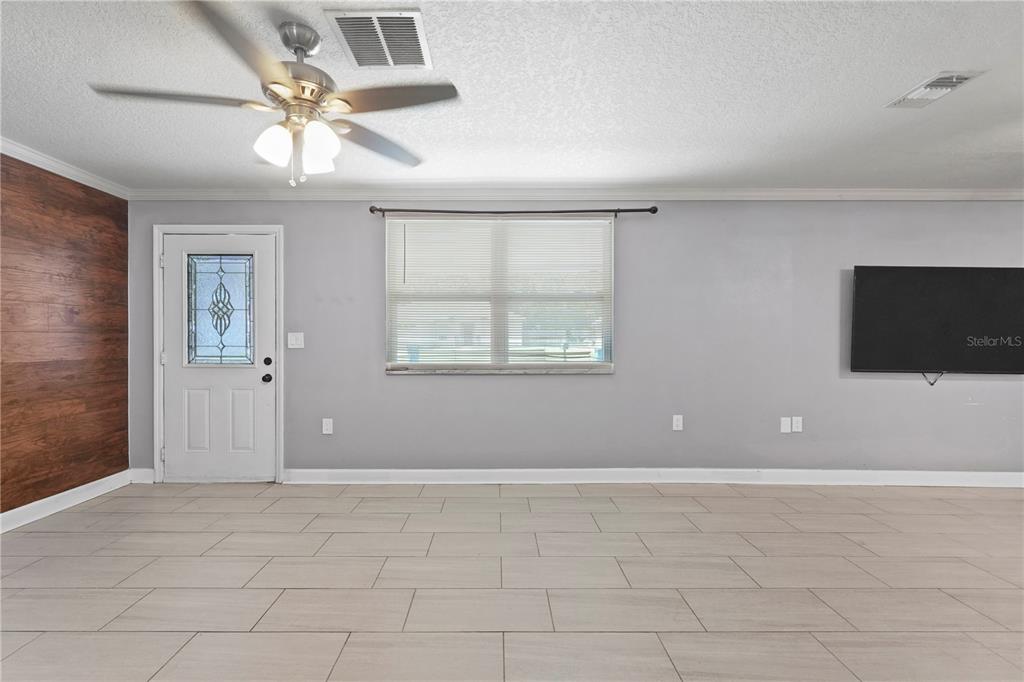 A living room features light tile flooring, gray walls, a ceiling fan, and a wood-paneled wall — 6290 PIEDMONT DRIVE, SPRING HILL, FL