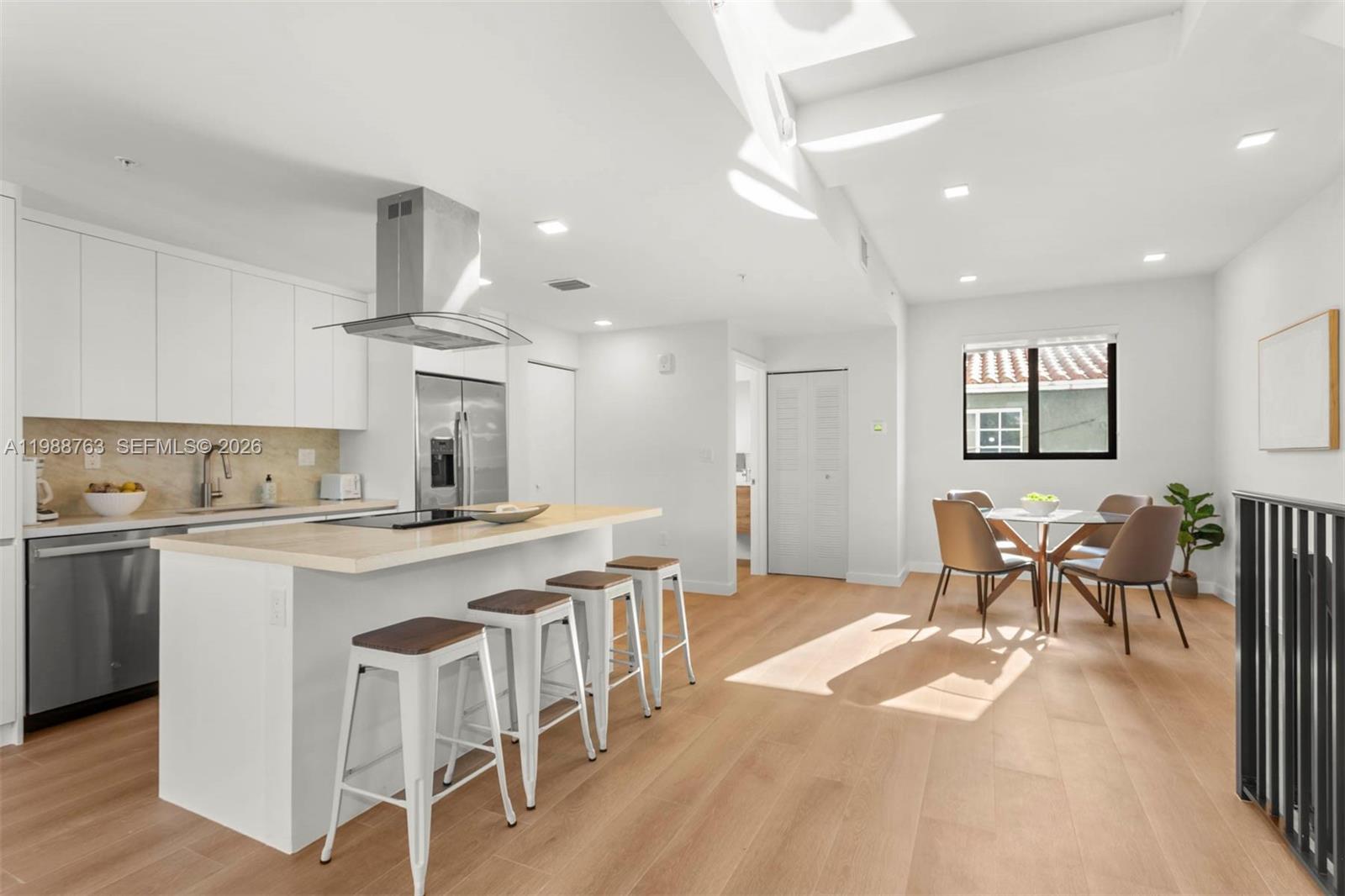 A modern kitchen features white cabinetry, a central island with bar seating, and dining area — 1376 SW 4th St # 7, Miami FL 33135, MIAMI, FL