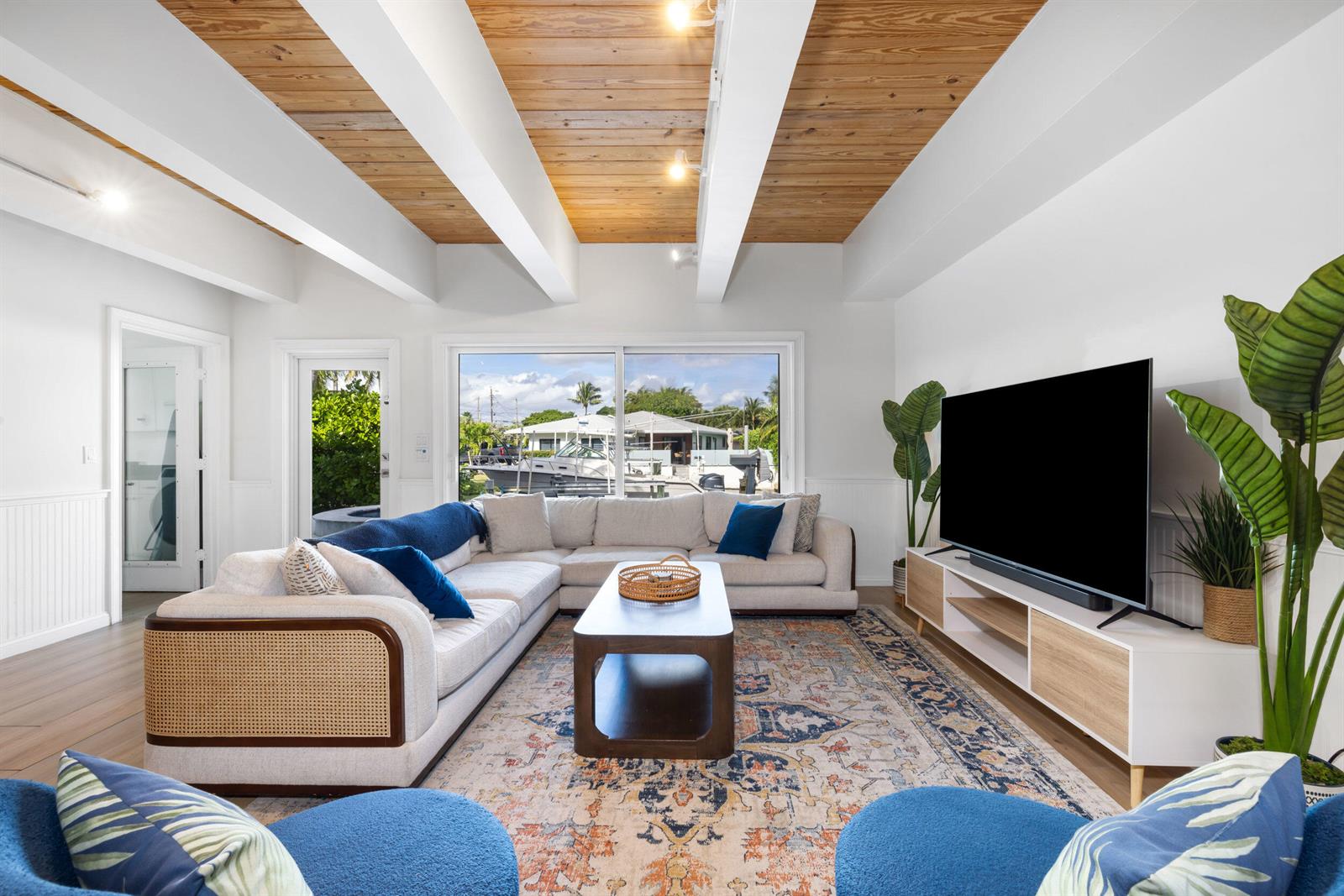 A living room features a sectional sofa, wood-paneled ceiling with beams, and a waterfront view — 100 Neptune Drive, Hypoluxo FL 33462, HYPOLUXO, FL