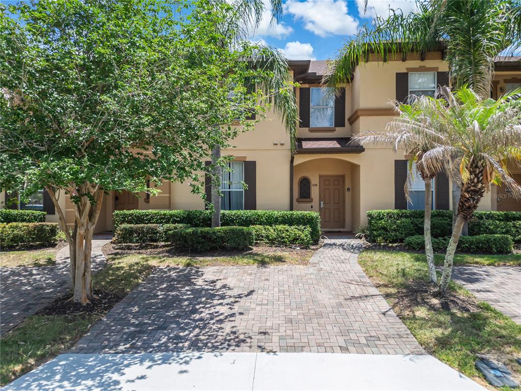 A two-story tan townhouse features a paved walkway, dark shutters, and a front door — 226 BERGAMO DRIVE, DAVENPORT, FL
