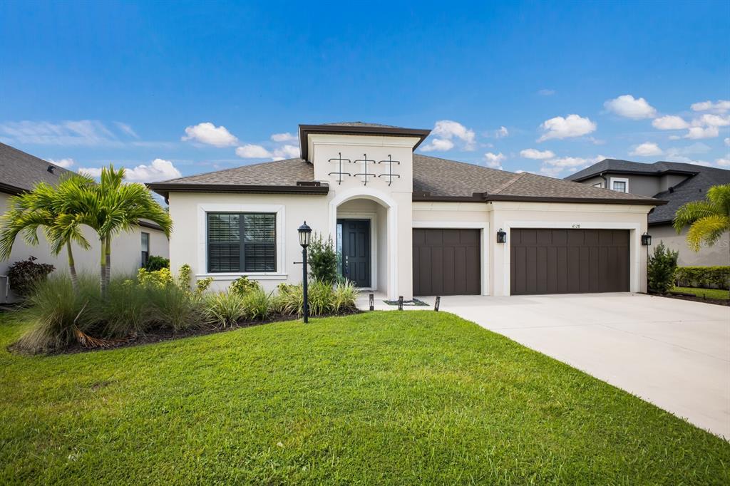 A single-story house with a beige stucco exterior, dark garage doors, and a front lawn — 4528 POND BROOK COURT, BRADENTON, FL