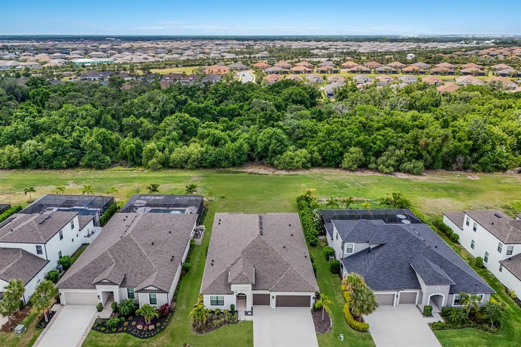 An aerial view shows three suburban houses with pools and a large wooded area behind them — 4528 POND BROOK COURT, BRADENTON, FL