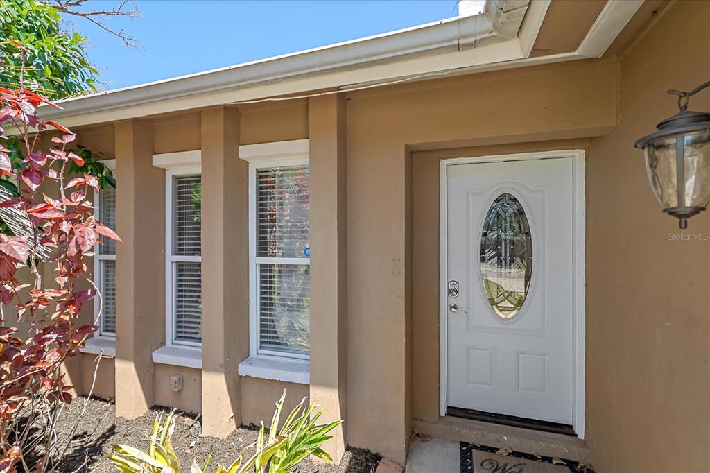 A tan exterior wall features a white front door with an oval glass insert — 3209 ASHTON ROAD, SARASOTA, FL