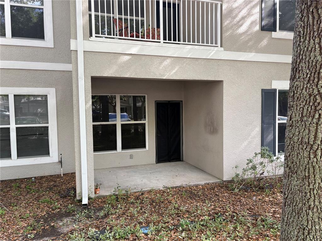 A ground-level concrete patio sits beneath a second-story balcony of a beige stucco building — 8009 HEMINGWAY CIRCLE UNIT 8009, HAINES CITY, FL