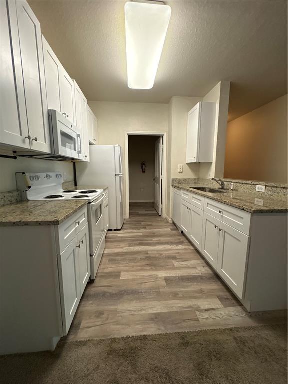 A galley-style kitchen features white cabinets, granite countertops, stainless steel appliances, and wood-look flooring — 8009 HEMINGWAY CIRCLE UNIT 8009, HAINES CITY, FL